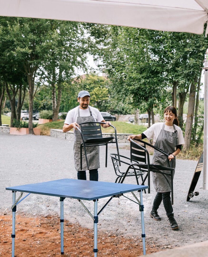 Two people standing next to a table and chairs.