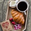 A tray with croissant, coffee and a card.