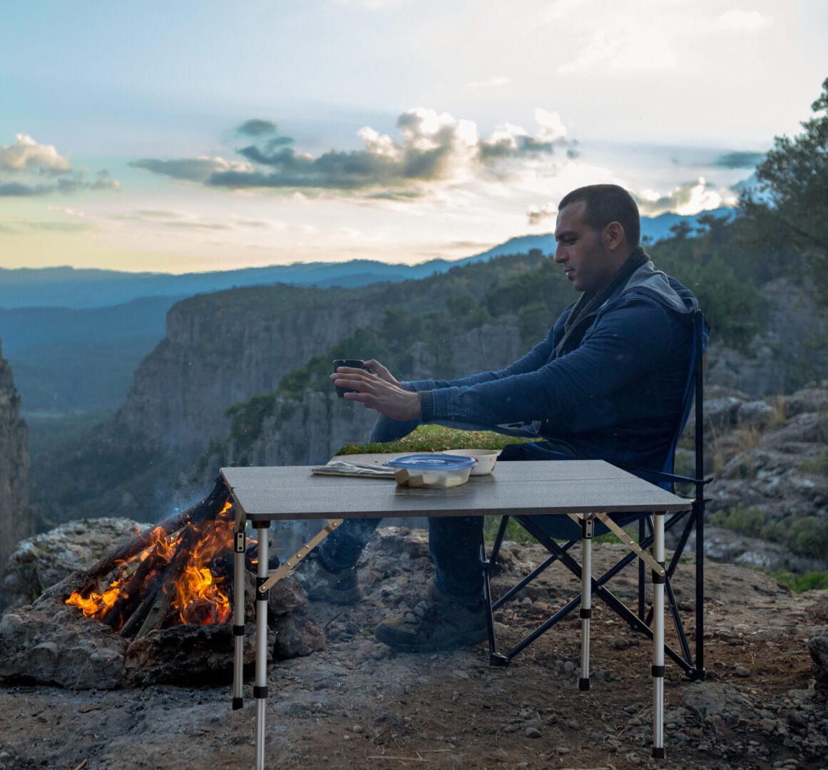 A man sitting at the top of a mountain near some fire.